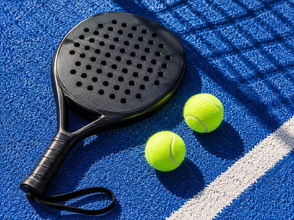 Black padel racket and two lime balls on a blue court